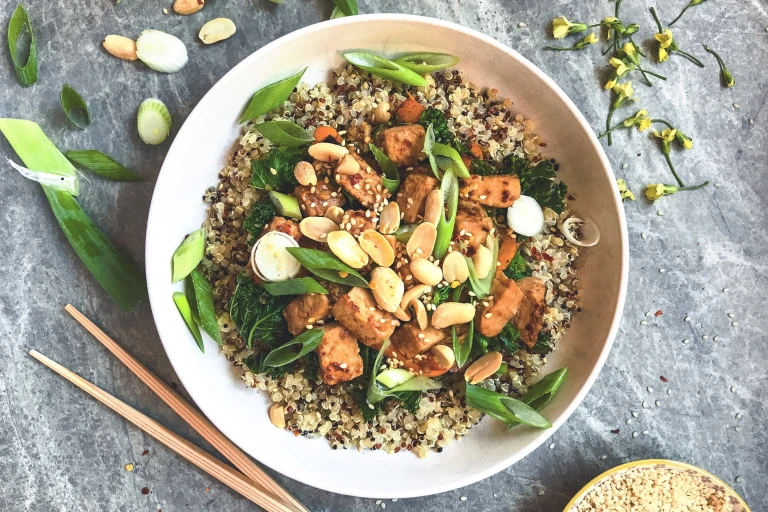 A bowl of quinoa topped with Quorn Pieces, kale, green onions, sesame seeds and peanuts.