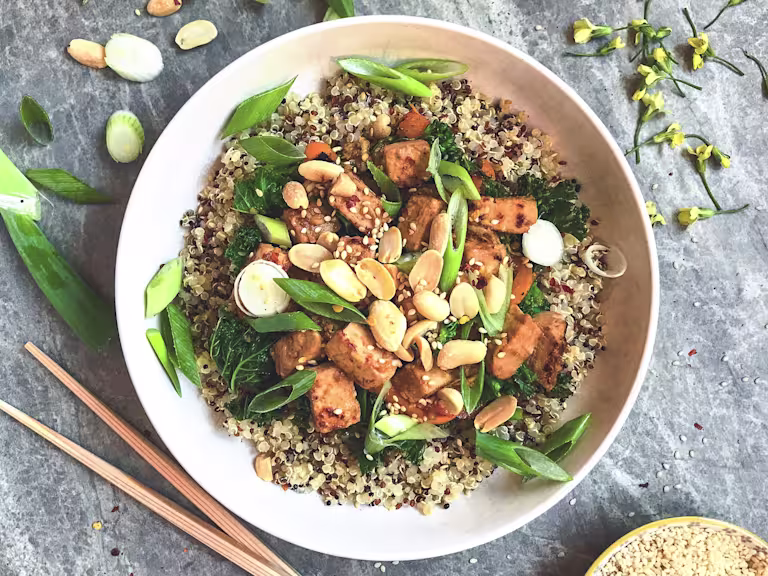 A bowl of quinoa topped with Quorn Pieces, kale, green onions, sesame seeds and peanuts.