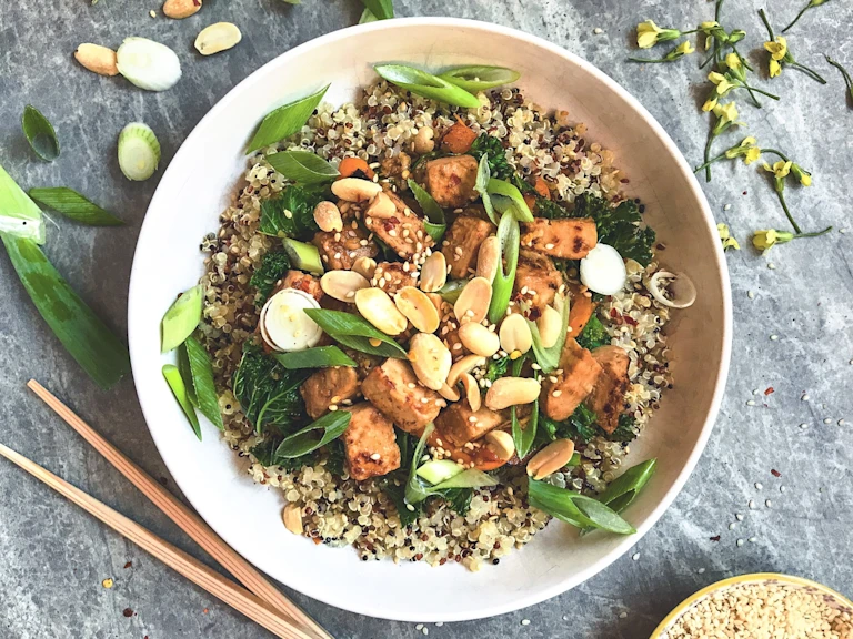 A bowl of quinoa topped with Quorn Pieces, kale, green onions, sesame seeds and peanuts.
