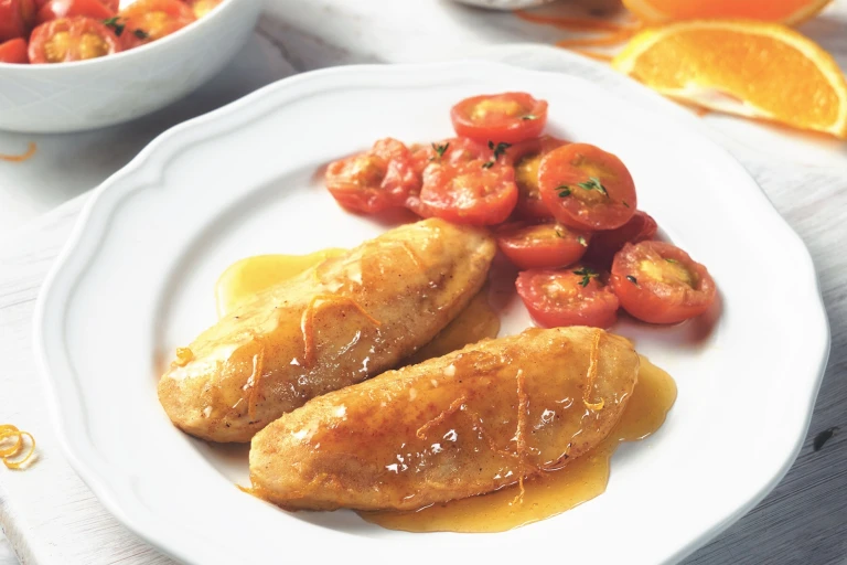 Quorn Fillets in an orange glaze with a side of cherry tomatoes on a white plate with an orange slice in the background.