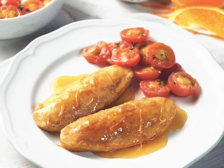 Quorn Fillets in an orange glaze with a side of cherry tomatoes on a white plate with an orange slice in the background.