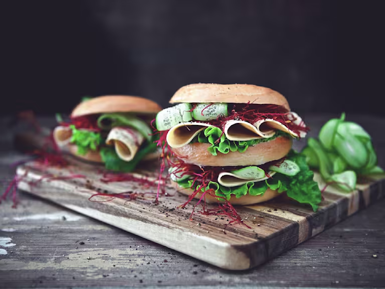 Healthy lunch idea of bagels filled with Quorn Vegan Chicken Free Slices, layered with salad served on a wooden board