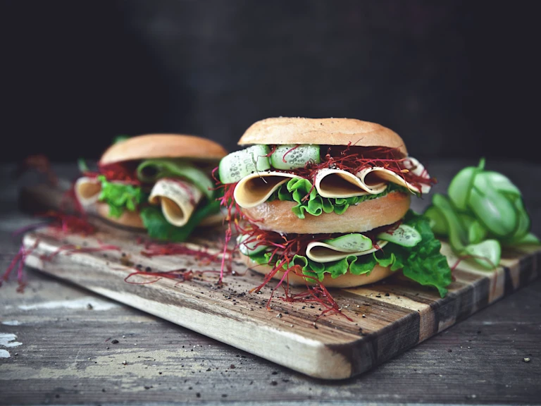 Healthy lunch idea of bagels filled with Quorn Vegan Chicken Free Slices, layered with salad served on a wooden board