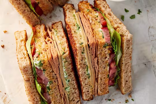 Quorn Vegan Club Sandwich cut into triangles facing upwards to show Quorn Chicken Slices and Quorn Finely Sliced Ham Style Slices with salad and tomato.