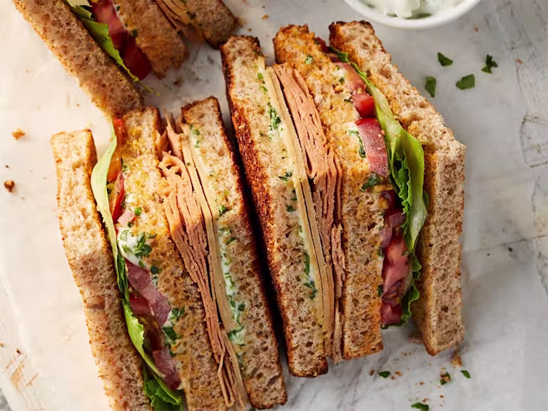 Quorn Vegan Club Sandwich cut into triangles facing upwards to show Quorn Chicken Slices and Quorn Finely Sliced Ham Style Slices with salad and tomato.