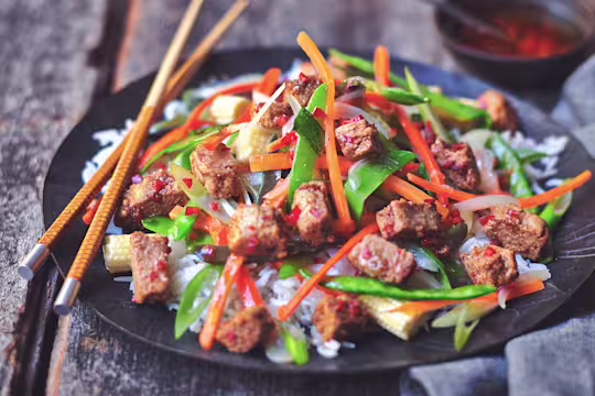 Healthy stir fry made with Quorn Vegan Pieces, mangetout and shredded carrot, served on a bed of rice on a plate with chopsticks