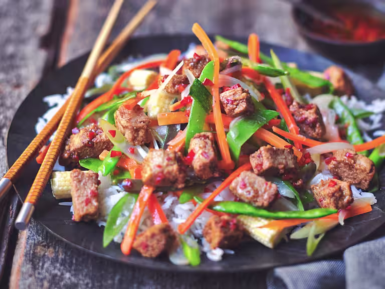 Healthy stir fry made with Quorn Vegan Pieces, mangetout and shredded carrot, served on a bed of rice on a plate with chopsticks
