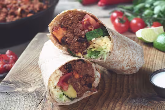 Vegetarian burrito sliced in half and stuffed with Quorn Mince, sweet potato, tomato and cheese served on a wooden board