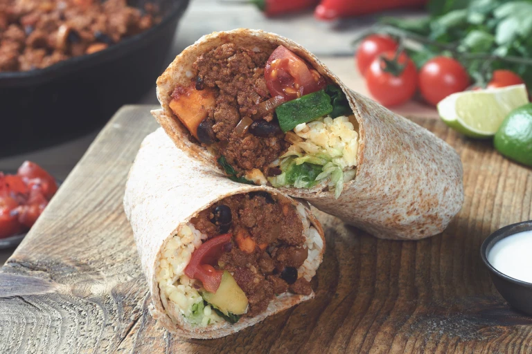 Vegetarian burrito sliced in half and stuffed with Quorn Mince, sweet potato, tomato and cheese served on a wooden board