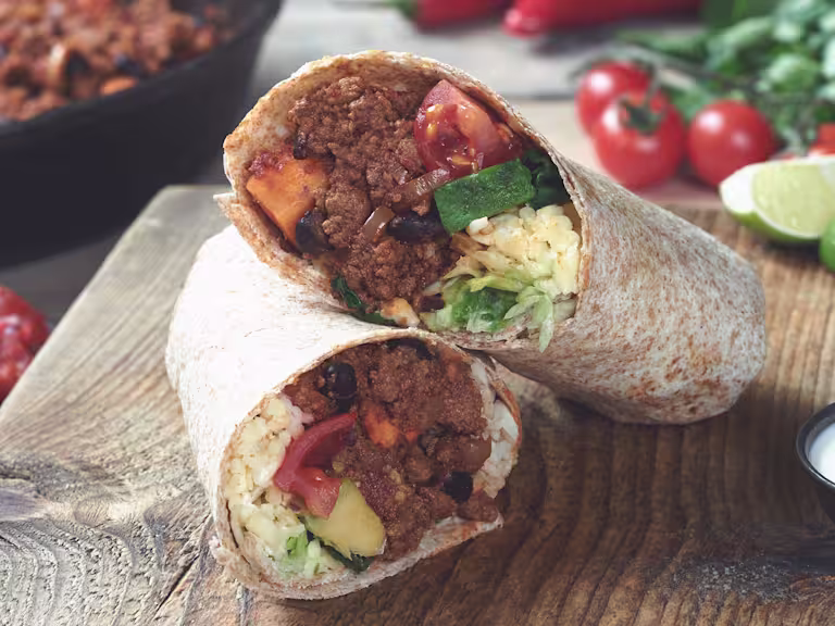 Vegetarian burrito sliced in half and stuffed with Quorn Mince, sweet potato, tomato and cheese served on a wooden board