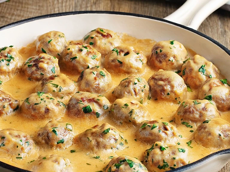 Creamy Swedish meatballs presented in a white oven dish 