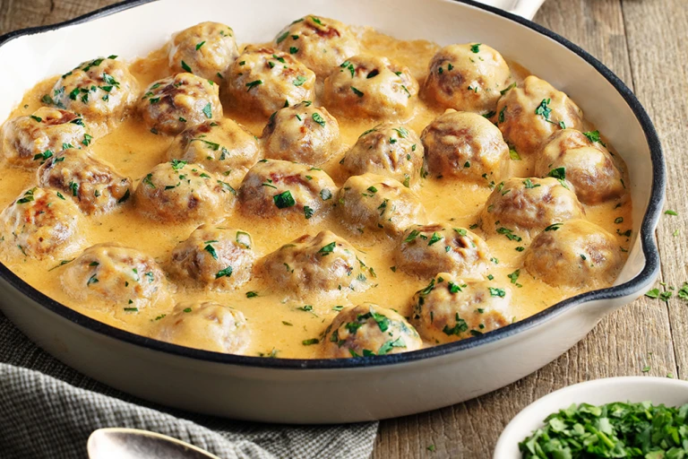 Creamy Swedish meatballs presented in a white oven dish 