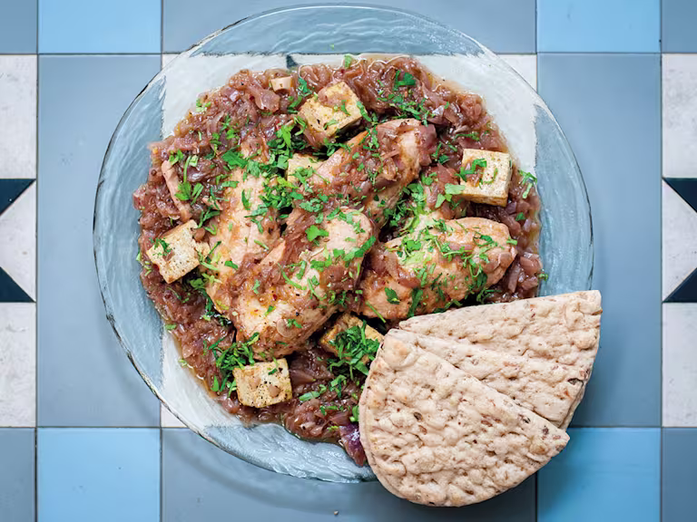 A glass bowl of doro wat made with Quorn Fillets on a blue tile background with two pieces of flatbread on the side.