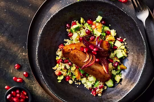 Two Quorn Sticky Glazed sausages topped with pomegranate seeds on a bed of pilaf cous-cous with a side serving of pomegranate seeds.