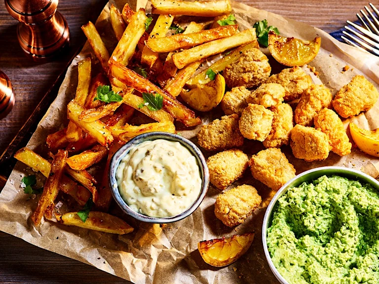 Quorn Vegan Fishless Scampi arranged on a board with chips, mushy peas, and tartare sauce on the side.