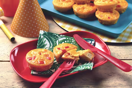 Mini vegetarian quiche with Quorn Pieces served on a leaf print napkin on a red plate with one quiche cut into with a piece on a fork