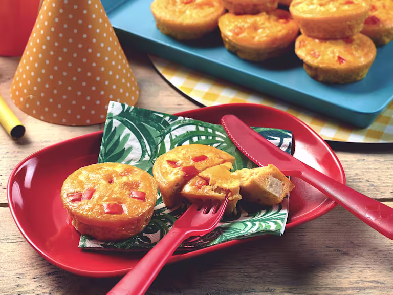 Mini vegetarian quiche with Quorn Pieces served on a leaf print napkin on a red plate with one quiche cut into with a piece on a fork