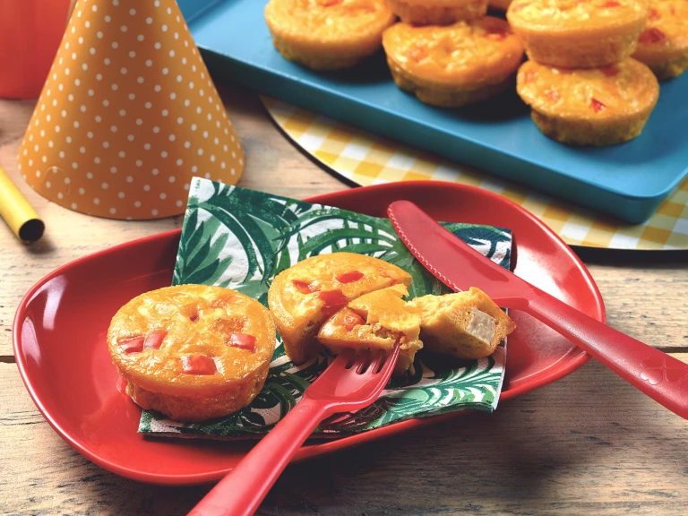 Mini vegetarian quiche with Quorn Pieces served on a leaf print napkin on a red plate with one quiche cut into with a piece on a fork