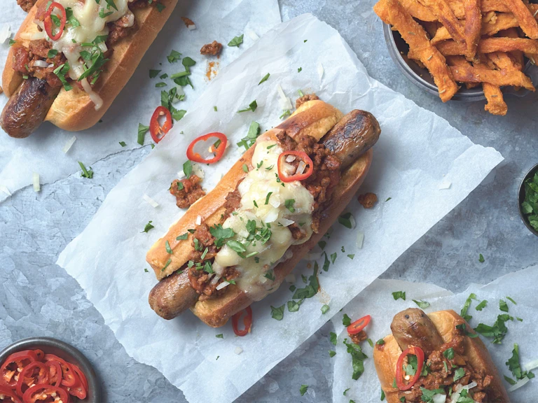 Vegetarian hot dogs using Quorn Sausages topped with Quorn Mince chilli, onions and red chilli served on parchment paper