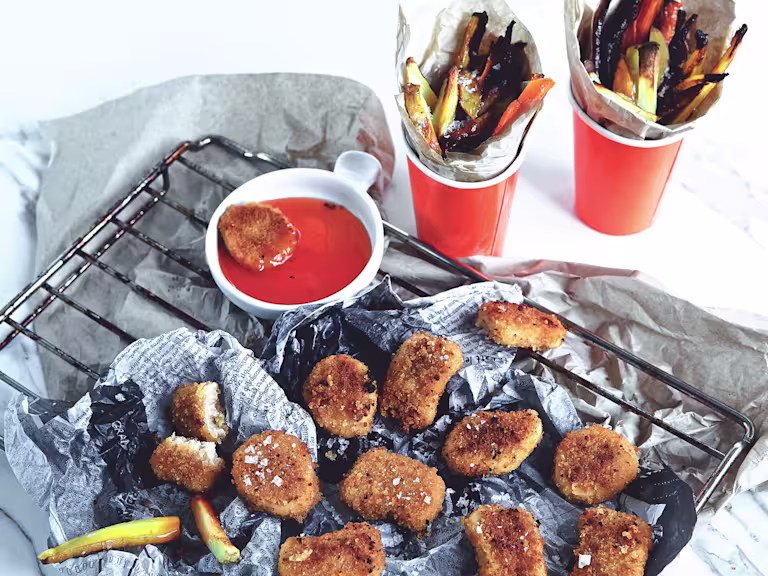 Quorn Vegan Nuggets served on newspaper on top of a wire rack with a side of orange sauce and cups of roasted root vegetables
