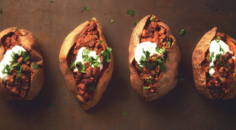 Four sweet potatoes split and stuffed with chili and topped with sour cream and parsley.