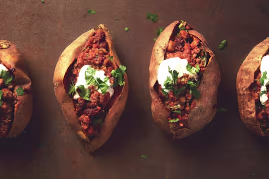 Four sweet potatoes split and stuffed with chili and topped with sour cream and parsley.