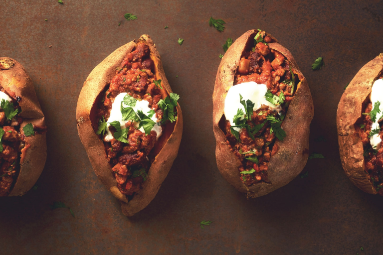 Four sweet potatoes split and stuffed with chili and topped with sour cream and parsley.