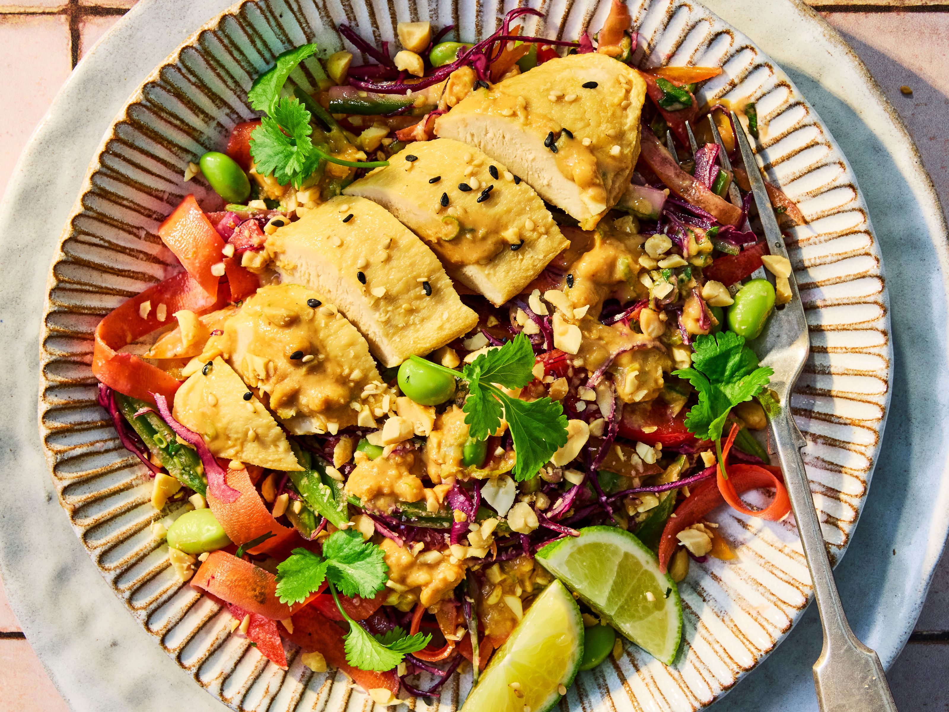 Quorn Satay Salad Bowl with Quorn Fillets, served with fresh vegetables, grains, herbs and a lime wedge.