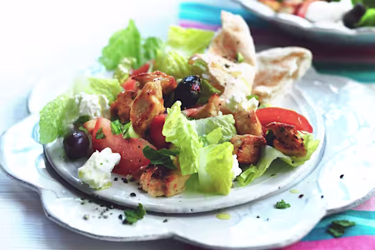 Romaine lettuce, feta cheese, sliced tomatoes, olives, and Quorn Pieces on a white plate with flatbread on the side.