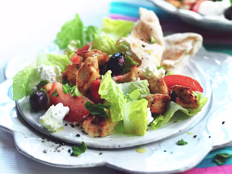 Romaine lettuce, feta cheese, sliced tomatoes, olives, and Quorn Pieces on a white plate with flatbread on the side.