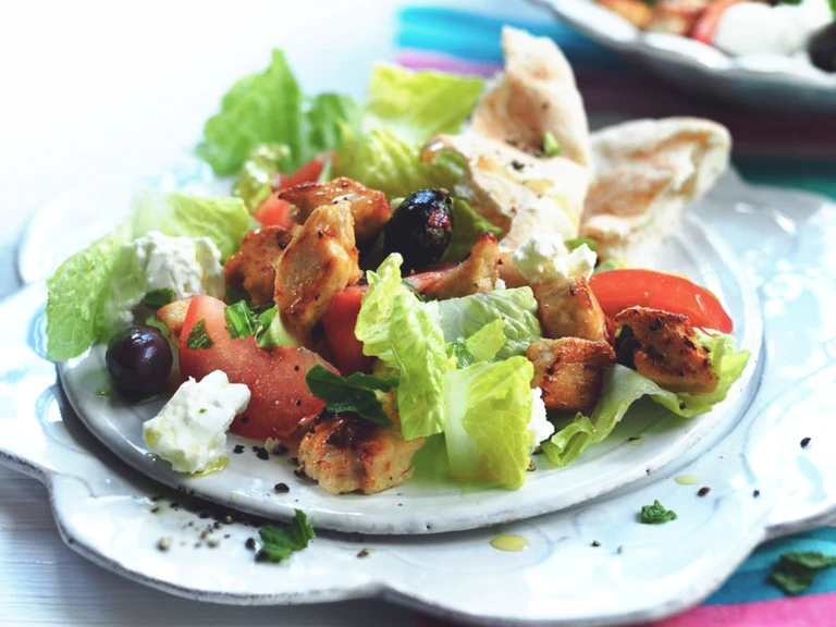 Romaine lettuce, feta cheese, sliced tomatoes, olives, and Quorn Pieces on a white plate with flatbread on the side.
