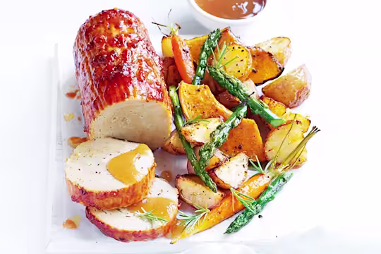 A plate of Quorn Roast baked in a tomato glaze with a side of roasted veggies and vegan gravy.