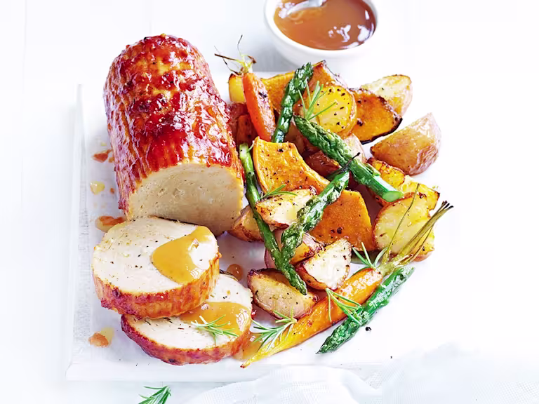 A plate of Quorn Roast baked in a tomato glaze with a side of roasted veggies and vegan gravy.