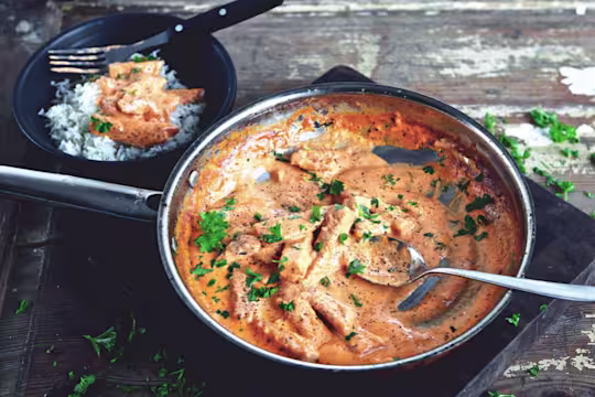 En stor portion Quorn vegetarisk Stroganoff serverad i en svart tallrik, med en sida av ris och toppad med vegetarisk stroganoff i bakgrunden