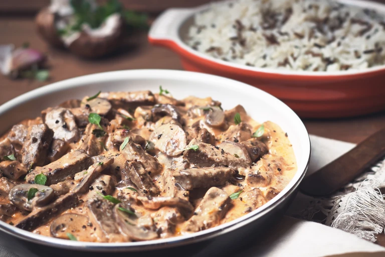 A serving of vegetarian stroganoff made with Quorn Vegetarian Steak Strips and mushrooms in a white dish with the baking dish in the background.