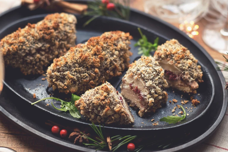 Three breaded Quorn Fillets with one sliced in thirds to reveal a cranberry-goat cheese filling on a black oblong plate.