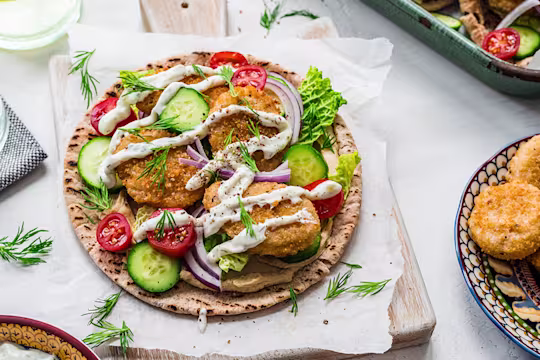 An open pita with Quorn meatless nuggets topped with sauces with a bowl of meatless nuggets on the side.