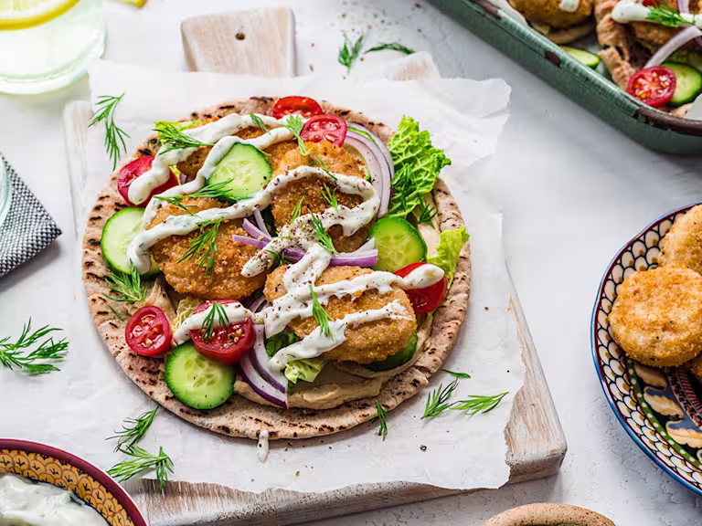 An open pita with Quorn meatless nuggets topped with sauces with a bowl of meatless nuggets on the side.