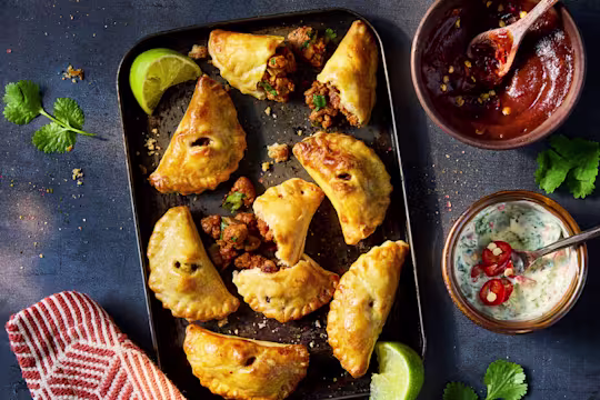 Vegetarian empanadas on a baking sheet with two side dips and lime wedge garnish.