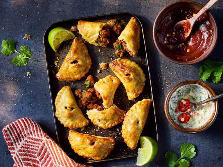 Vegetarian empanadas on a baking sheet with two side dips and lime wedge garnish.