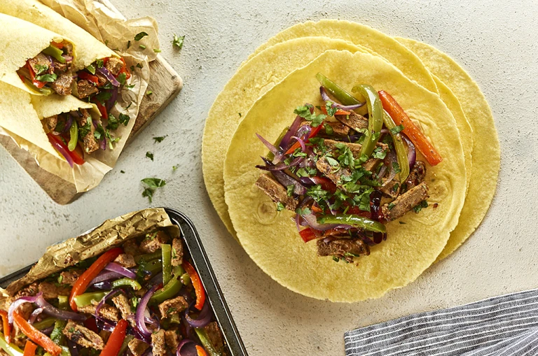 Open vegetarian fajita wraps with filling next to closed wraps and baking tray of filling