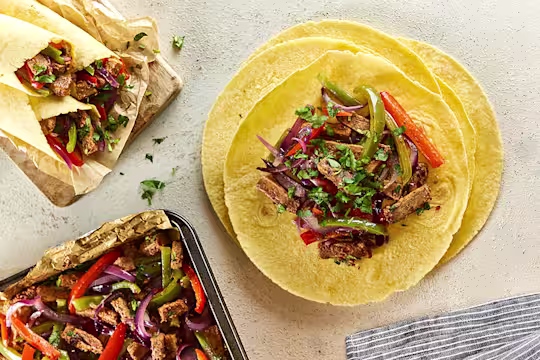 Open vegetarian fajita wraps with filling next to closed wraps and baking tray of filling