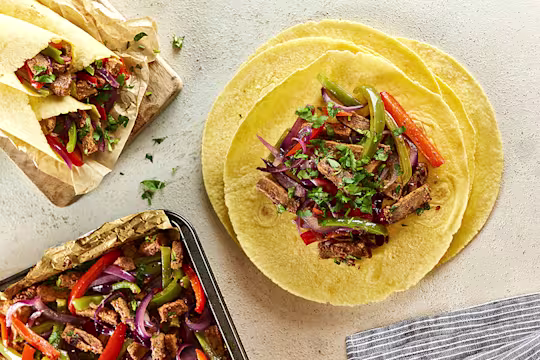 Open vegetarian fajita wraps with filling next to closed wraps and baking tray of filling