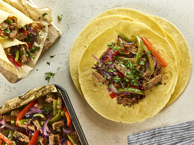 Open vegetarian fajita wraps with filling next to closed wraps and baking tray of filling