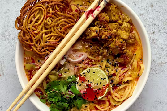 Khao Soi served in a white bowl with Quorn Pieces, noodles and lime and coriander garnish with wooden chopsticks.