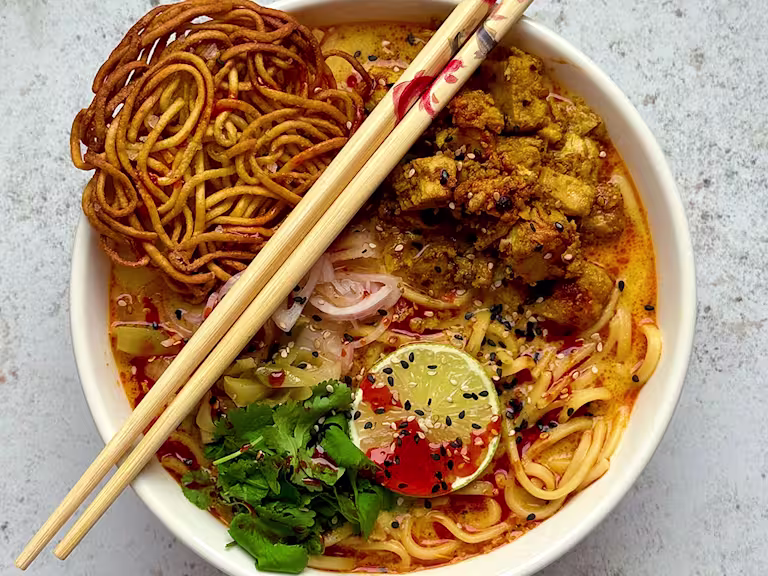 Khao Soi served in a white bowl with Quorn Pieces, noodles and lime and coriander garnish with wooden chopsticks.