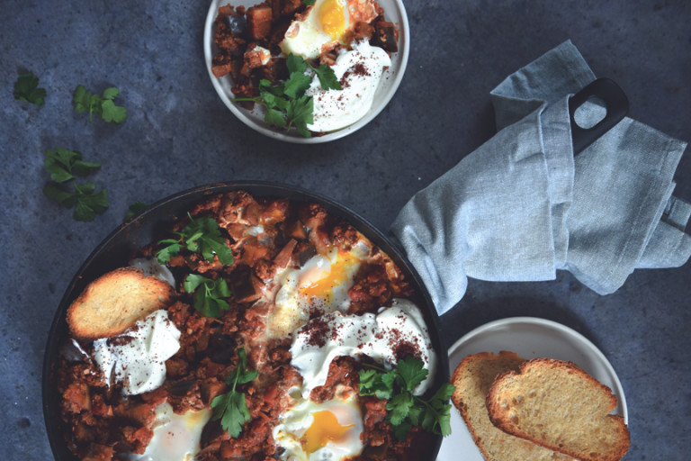 Shakshuka of Quorn Mince and aubergine and eggs, served in a dish next to a plate of toasts and a serving of shakshuka