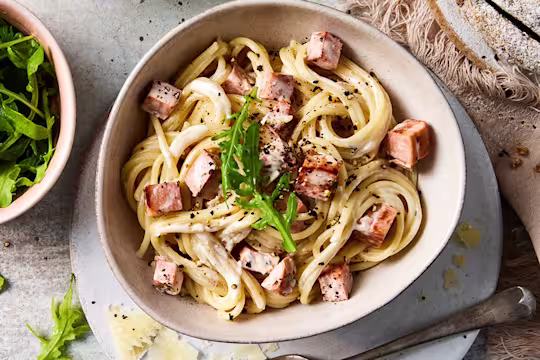 A bowl of vegetarian spaghetti pasta carbonara with diced Quorn Vegetarian Ham Roast and a side of rocket leaves.