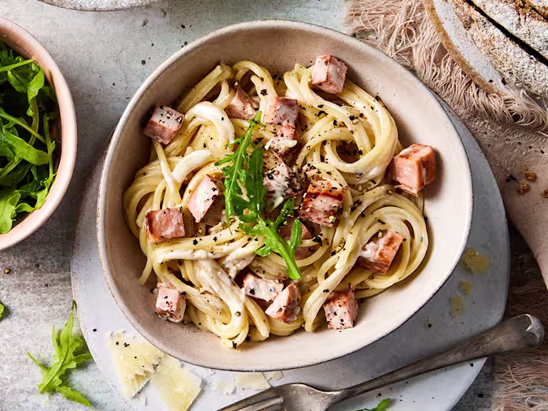 A bowl of vegetarian spaghetti pasta carbonara with diced Quorn Vegetarian Ham Roast and a side of rocket leaves.