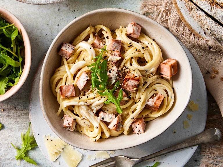 A bowl of vegetarian spaghetti pasta carbonara with diced Quorn Vegetarian Ham Roast and a side of rocket leaves.